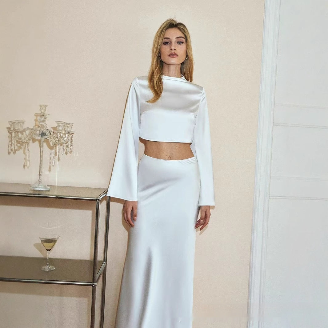 Woman in a white outfit standing in a room with a glass table and candle holder.