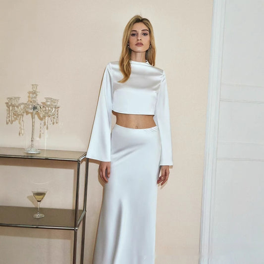 Woman in a white outfit standing in a room with a glass table and candle holder.
