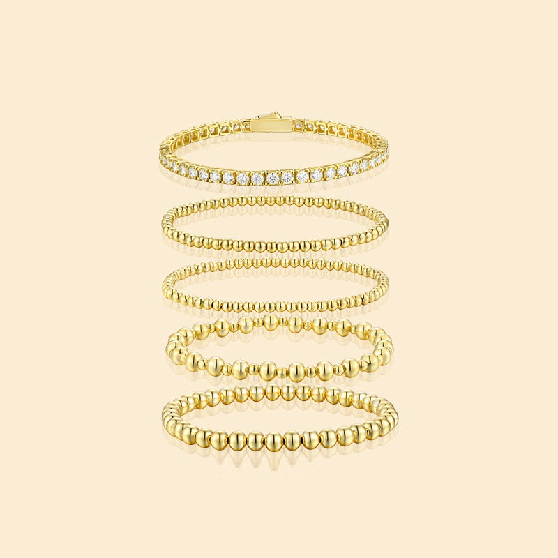 Set of gold bracelets with clear stones on a beige background