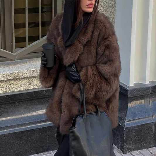 Person wearing a brown fur coat and holding a black handbag on a city street.