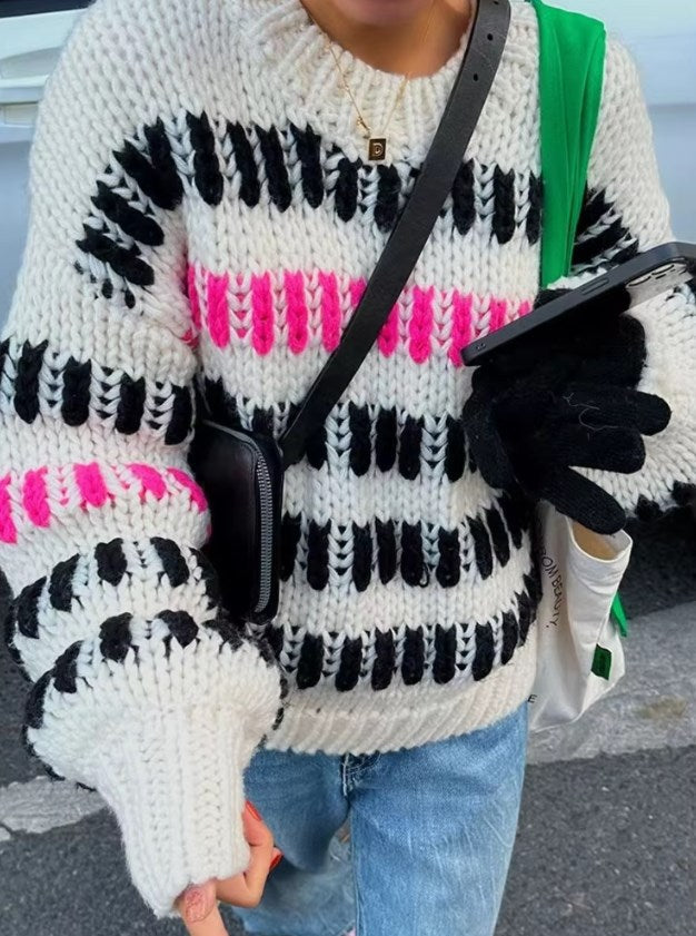 Person wearing a patterned sweater with black, white, and pink colors, holding a phone.