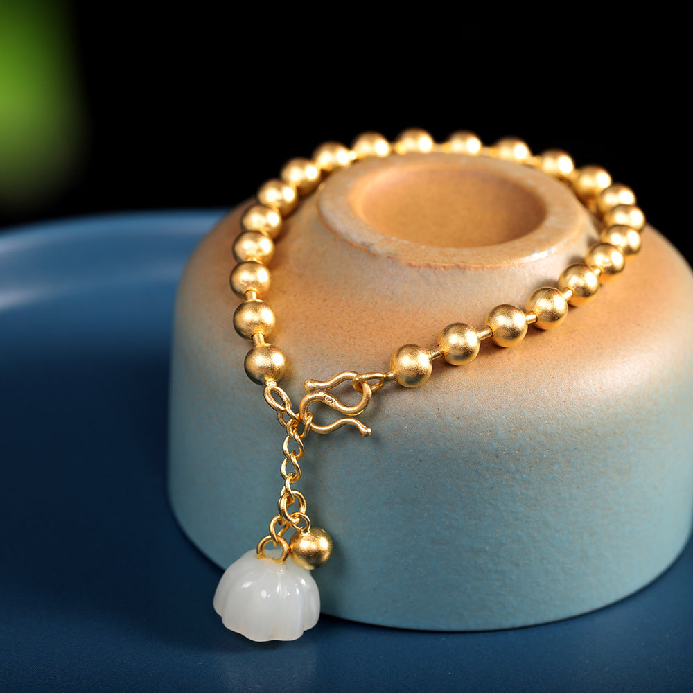 Gold beaded bracelet with a white charm on a wooden stand