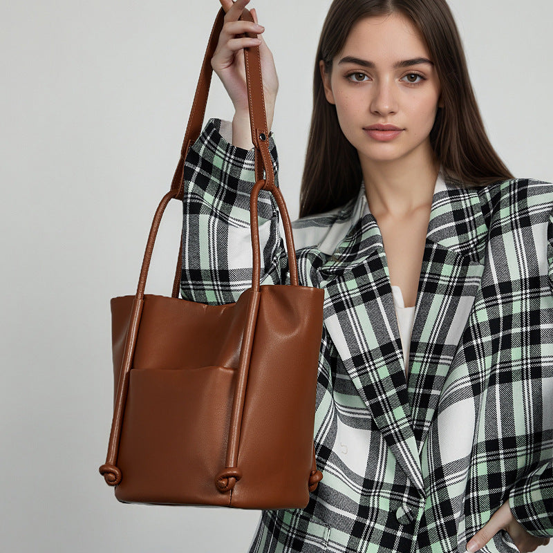 Woman holding a brown leather handbag against a plain background