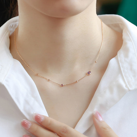 Rose gold necklace with pink gemstones worn by a person in a white shirt.
