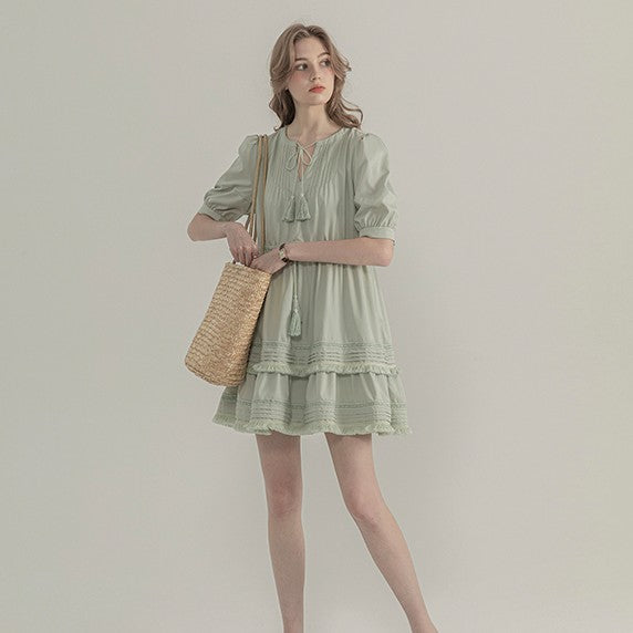 Woman wearing a light green dress holding a straw bag against a plain background