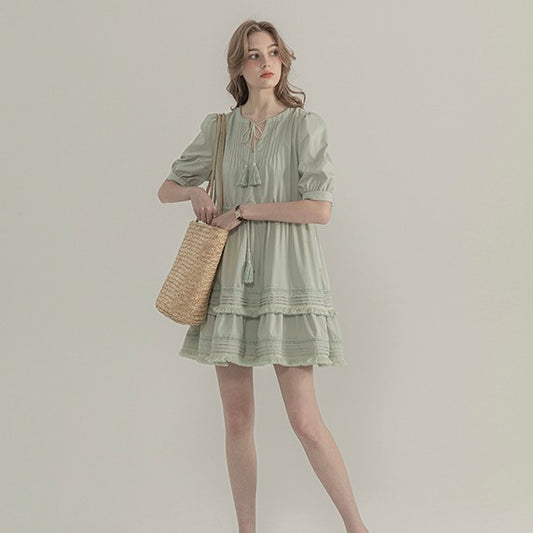 Woman wearing a light green dress holding a straw bag against a plain background