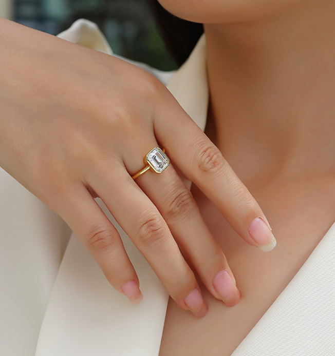 Close-up of a hand wearing a gold ring with a diamond on a blurred background