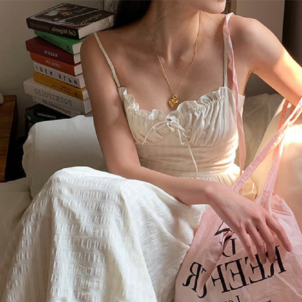 Woman in a white dress sitting on a bed with books stacked in the background