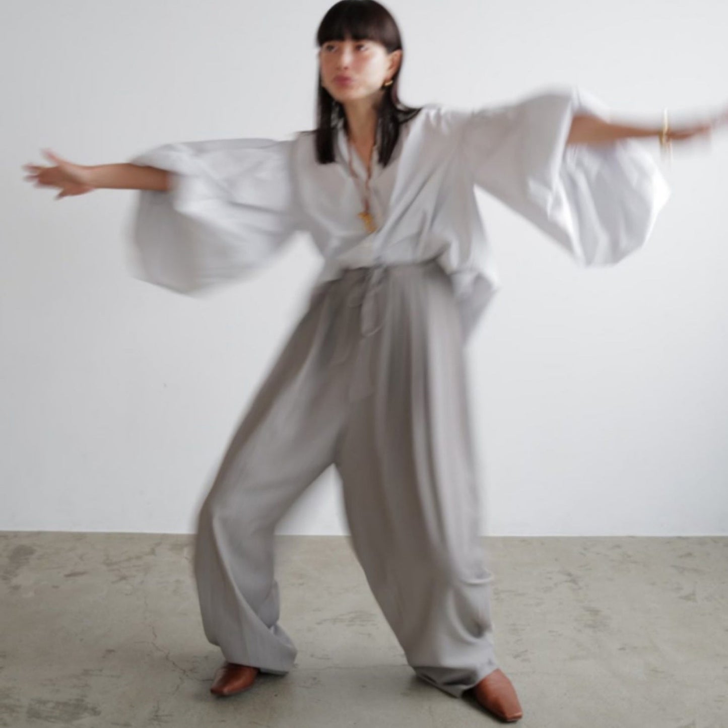 Person wearing a loose-fitting white top and gray pants against a plain background