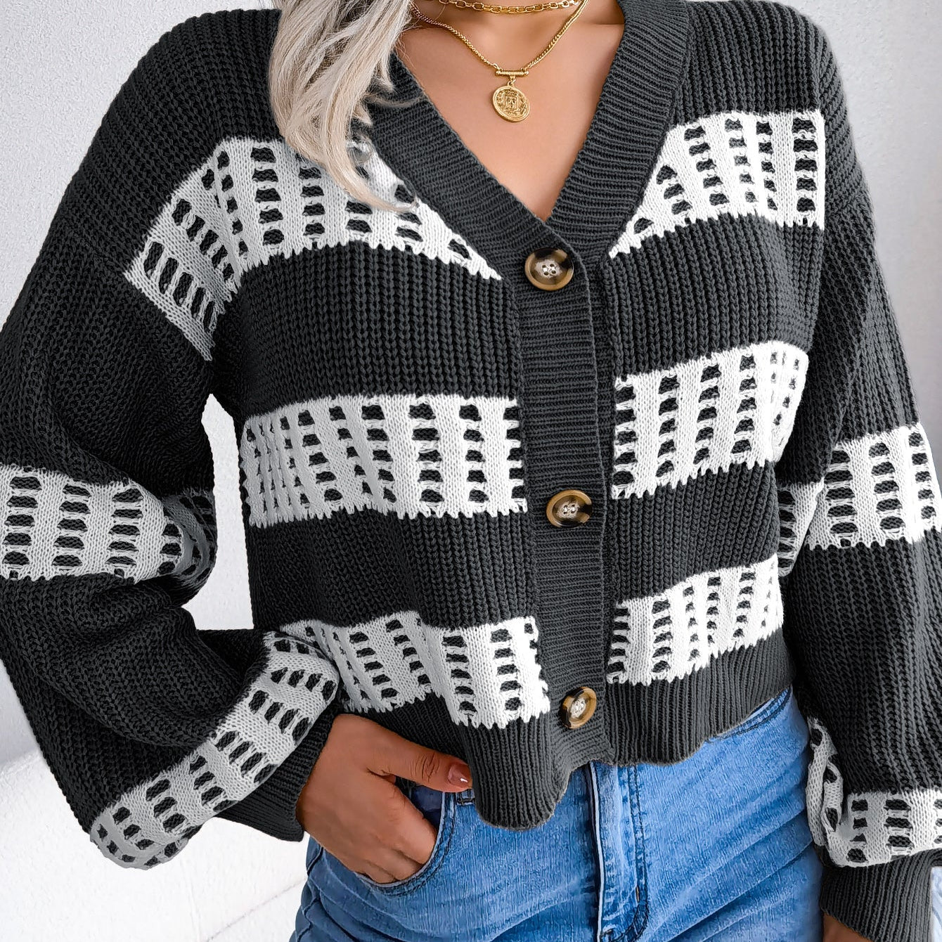 Person wearing a black and white patterned cardigan with blue jeans against a neutral background