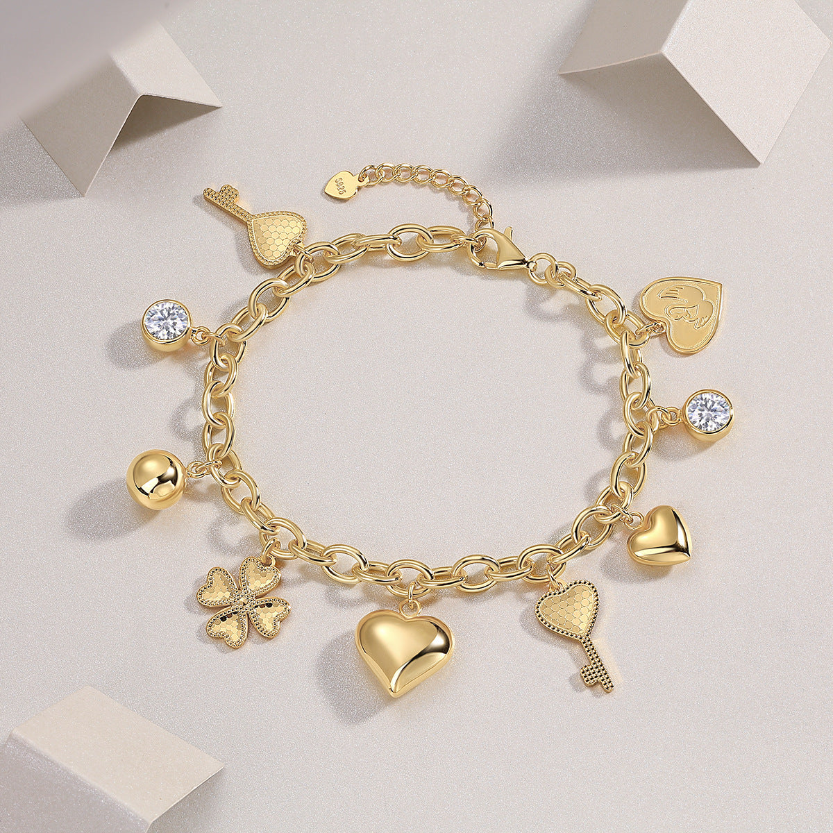 Gold charm bracelet with various charms on a light gray background