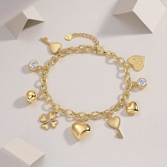 Gold charm bracelet with various charms on a light gray background