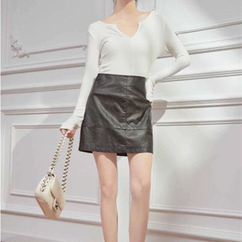 Person wearing a white sweater and black leather skirt holding a beige handbag against a light gray background