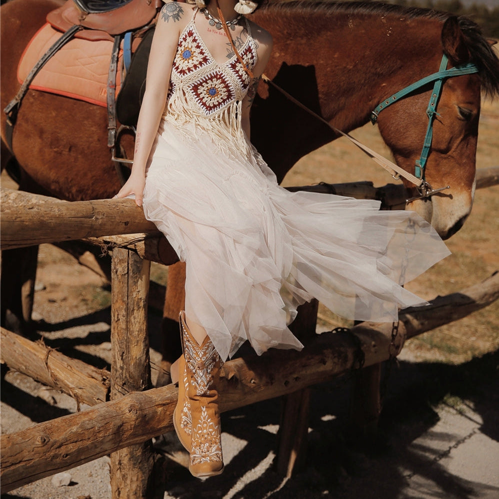 Woman in a white dress and straw hat sitting on a wooden fence with a horse in the background.