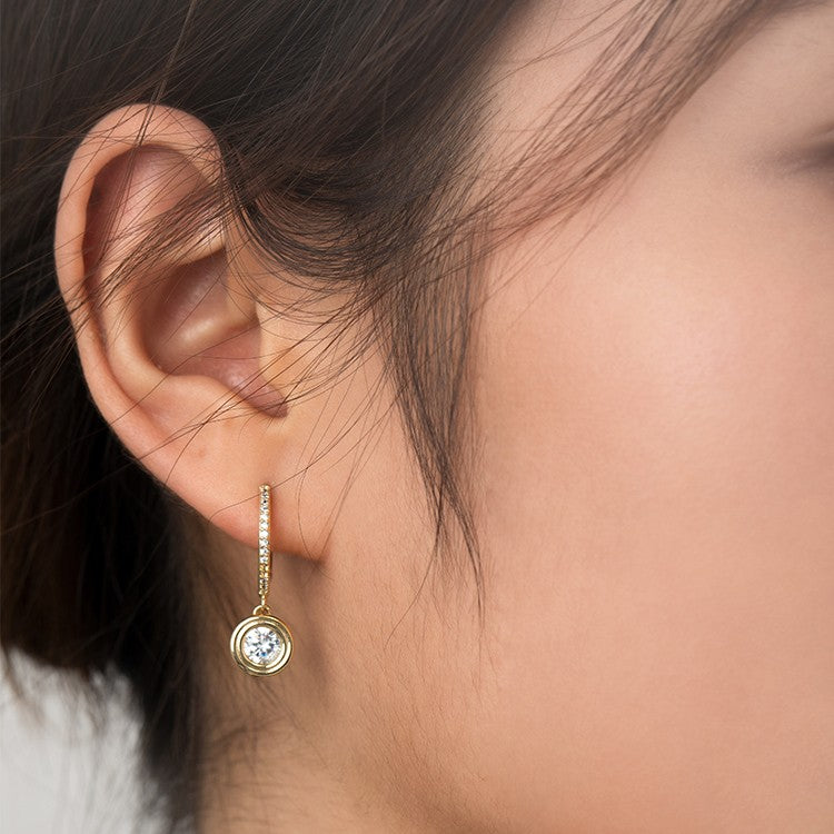 Gold earring with a clear gemstone worn by a person