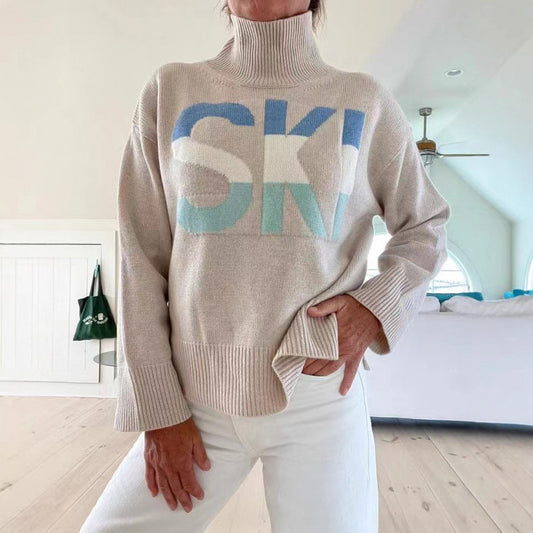 Person wearing a beige sweater with 'SKI' text in blue and green, standing in a room.