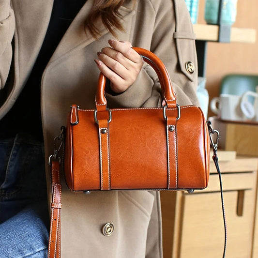 Brown leather handbag held by a person wearing a beige coat.