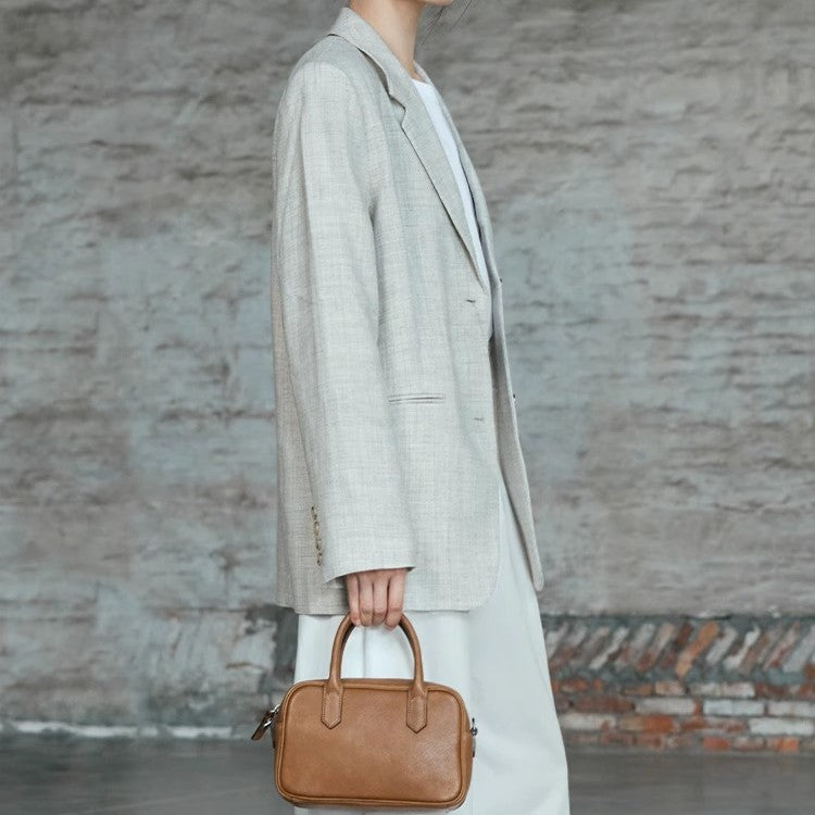 Person wearing a long coat holding a brown handbag against a textured wall.