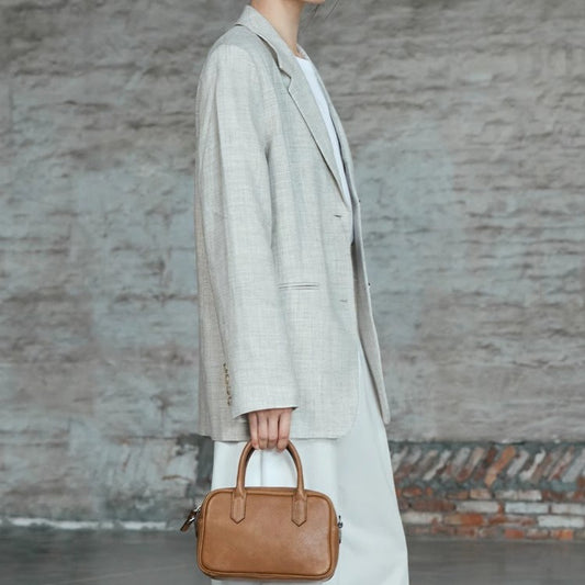 Person wearing a long coat holding a brown handbag against a textured wall.