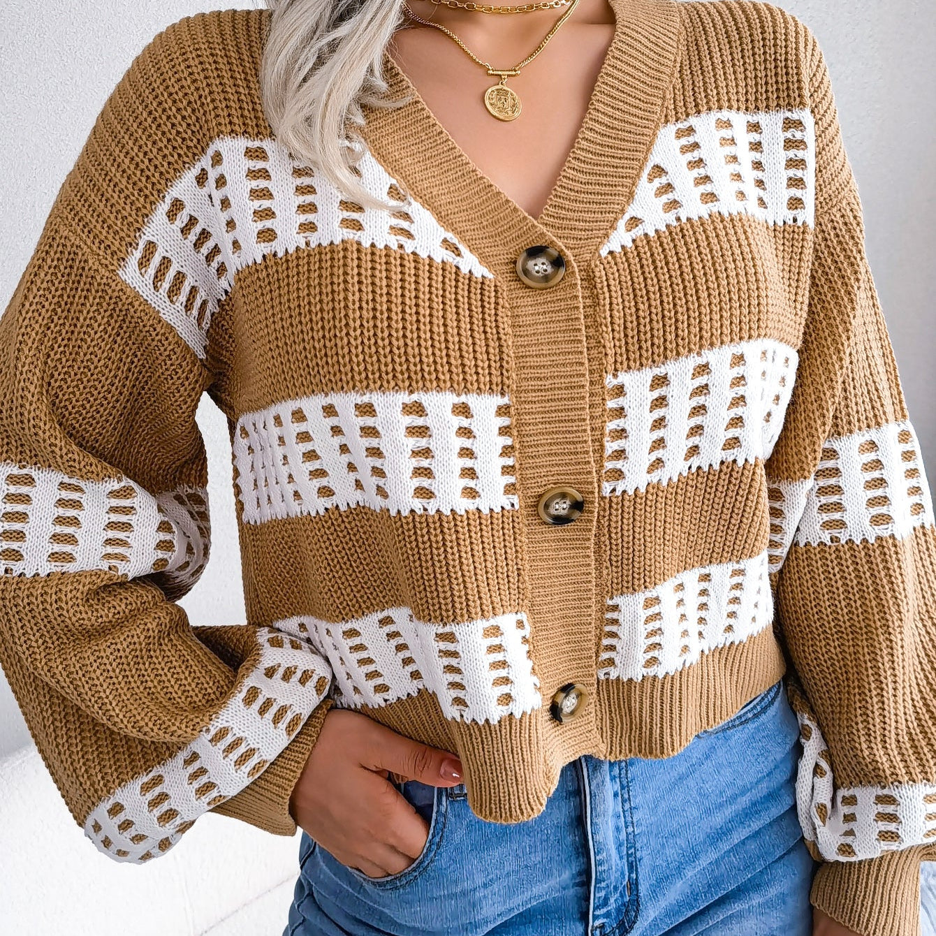 Person wearing a brown and white patterned cardigan with blue jeans on a plain background