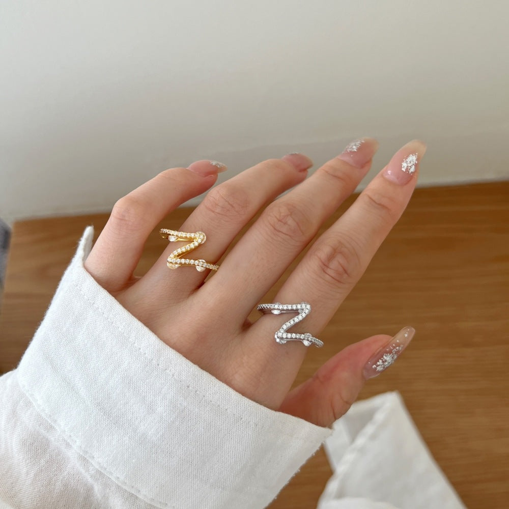 Hand wearing two rings with decorative designs on a neutral background