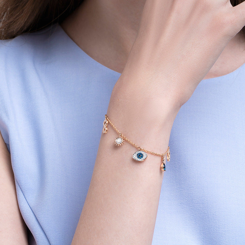 Close-up of a wrist wearing a delicate bracelet with small charms against a light blue background