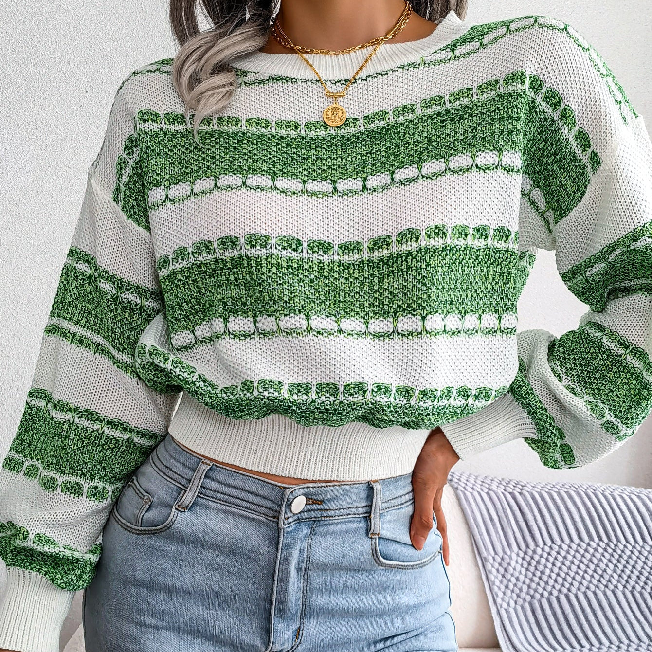 Person wearing a green and white striped sweater and blue jeans indoors.