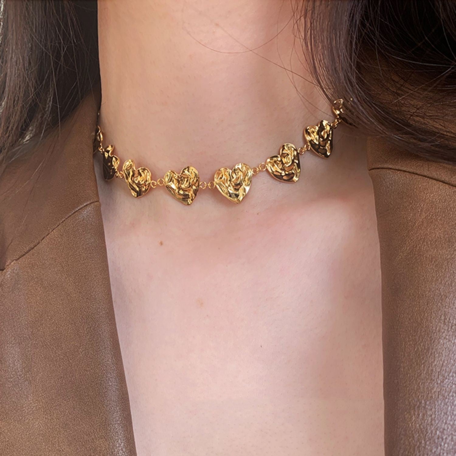 Gold necklace with heart-shaped pendants on a person wearing a brown jacket.