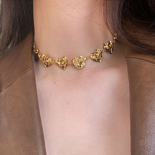 Gold necklace with heart-shaped pendants on a person wearing a brown jacket.