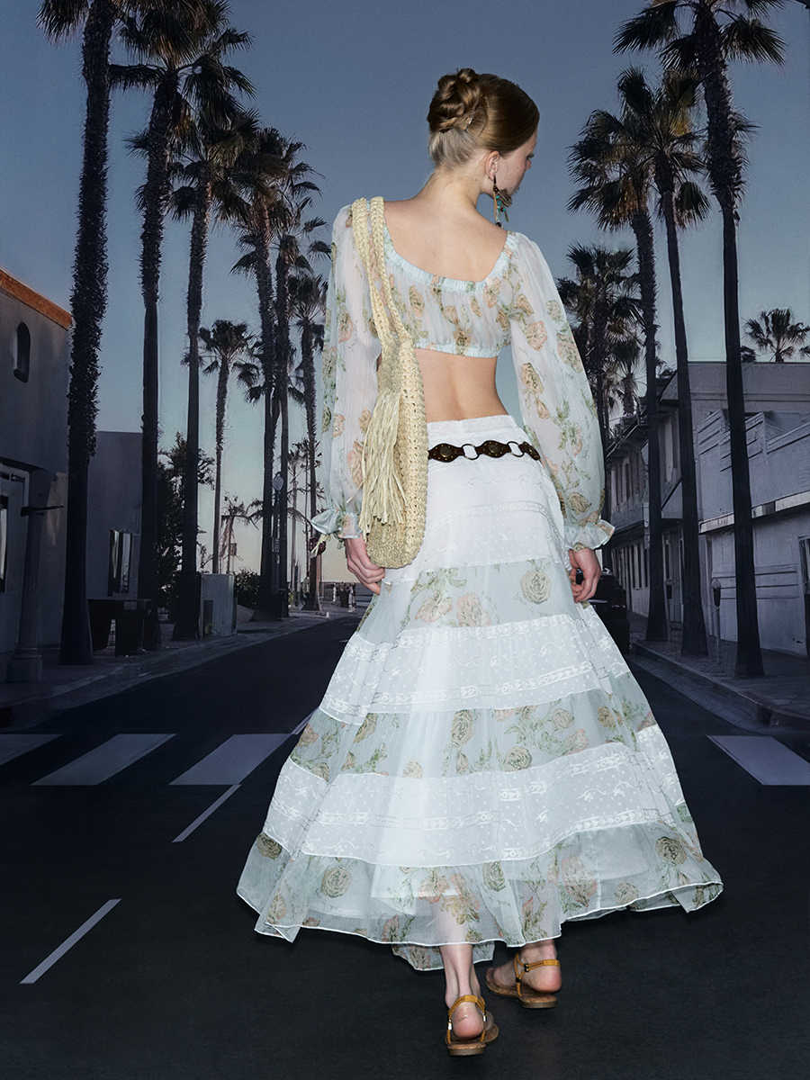 Woman in a floral dress walking on a street with palm trees in the background