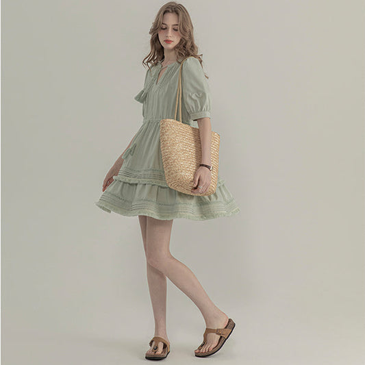 Woman in a green dress holding a straw bag on a plain background