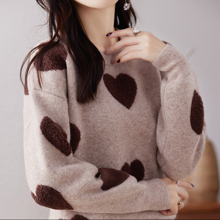 Person wearing a beige sweater with brown heart patterns on a plain background