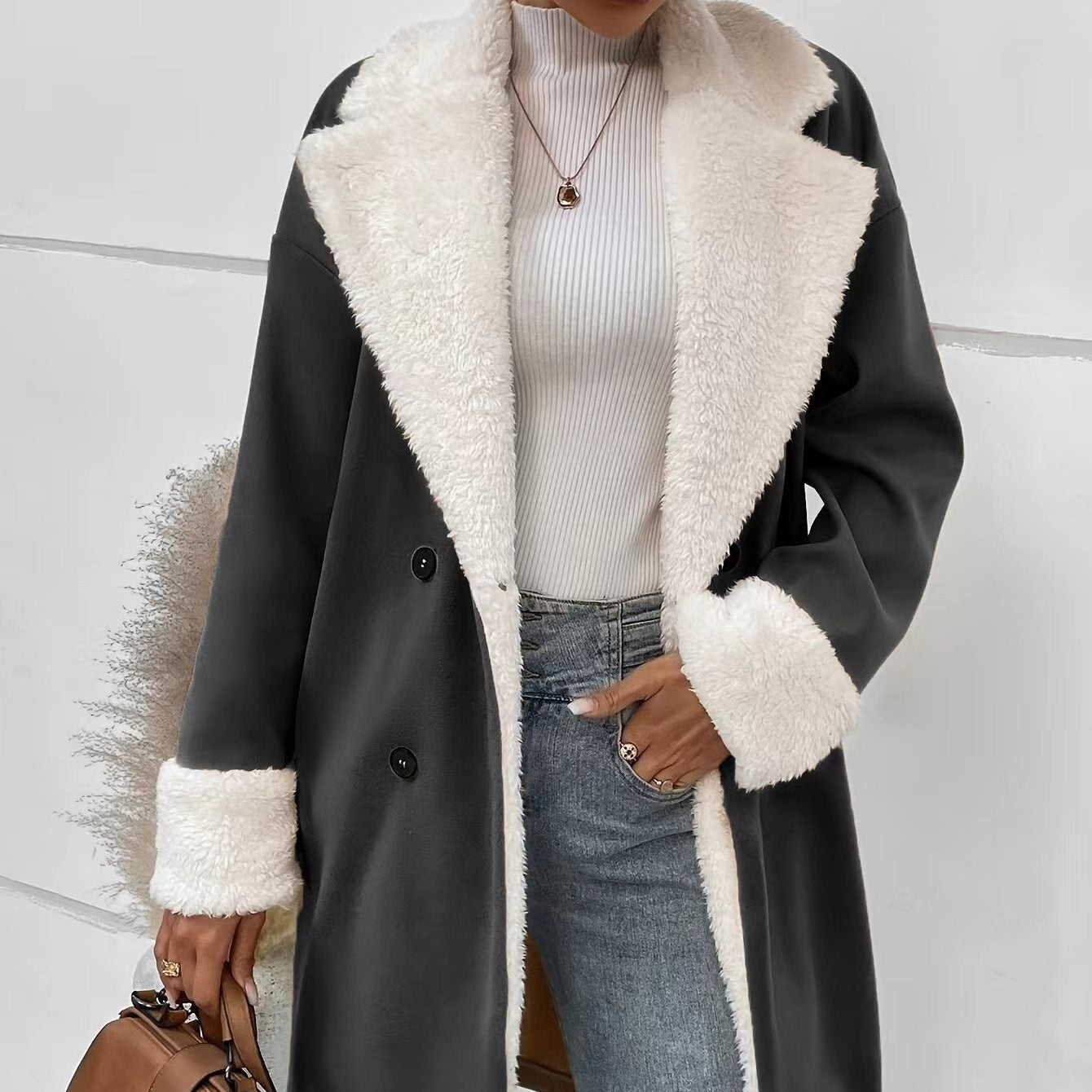 Person wearing a black coat with white fur trim, holding a brown handbag against a light background.