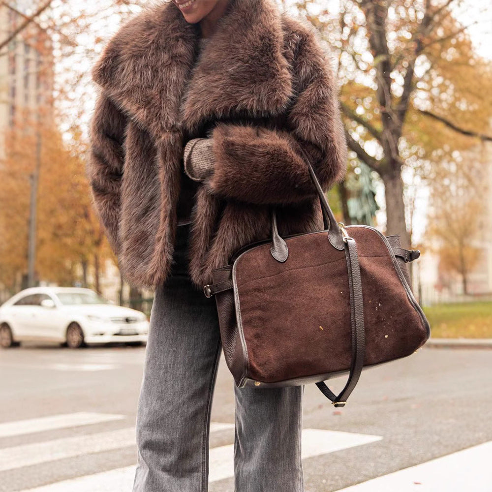 Person wearing a brown fur coat holding a matching brown leather bag on a street with trees in the background.