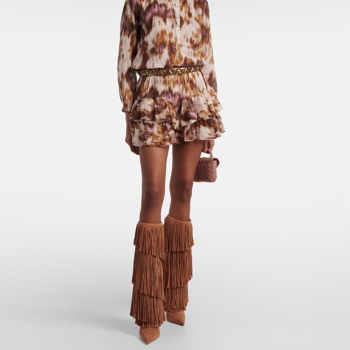 Person wearing a patterned dress with ruffled layers and brown fringe boots on a white background