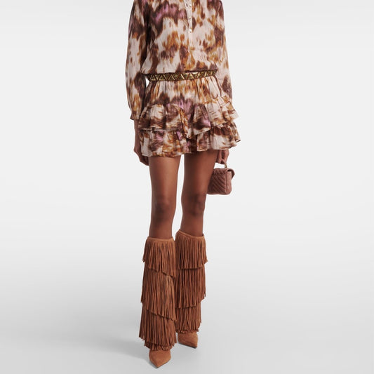 Person wearing a patterned dress with ruffled layers and brown fringe boots on a white background
