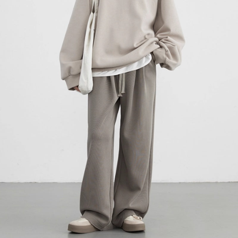 Person wearing a beige hoodie and pants with a white shirt underneath on a plain background