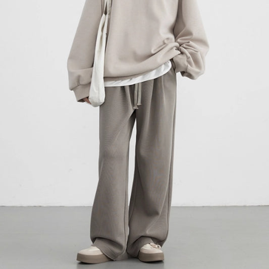 Person wearing a beige hoodie and pants with a white shirt underneath on a plain background