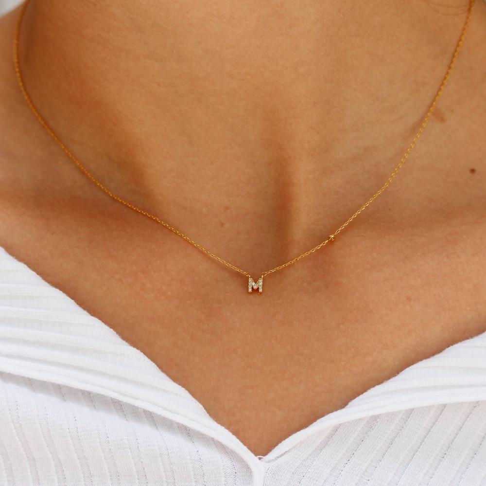 Gold necklace with a 'M' pendant on a person wearing a white top.