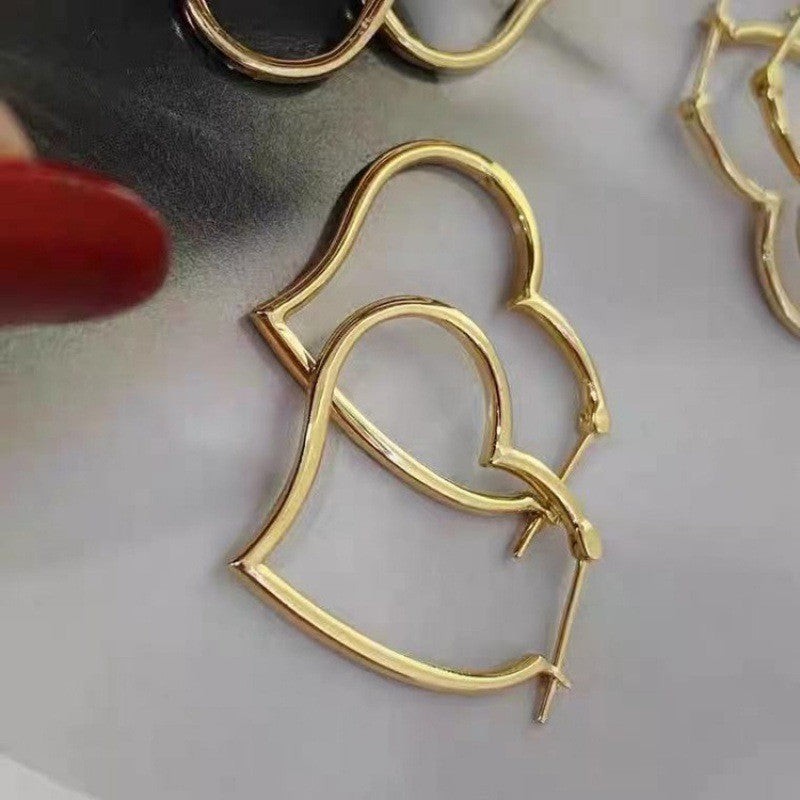 Gold heart-shaped hoop earrings on a reflective surface