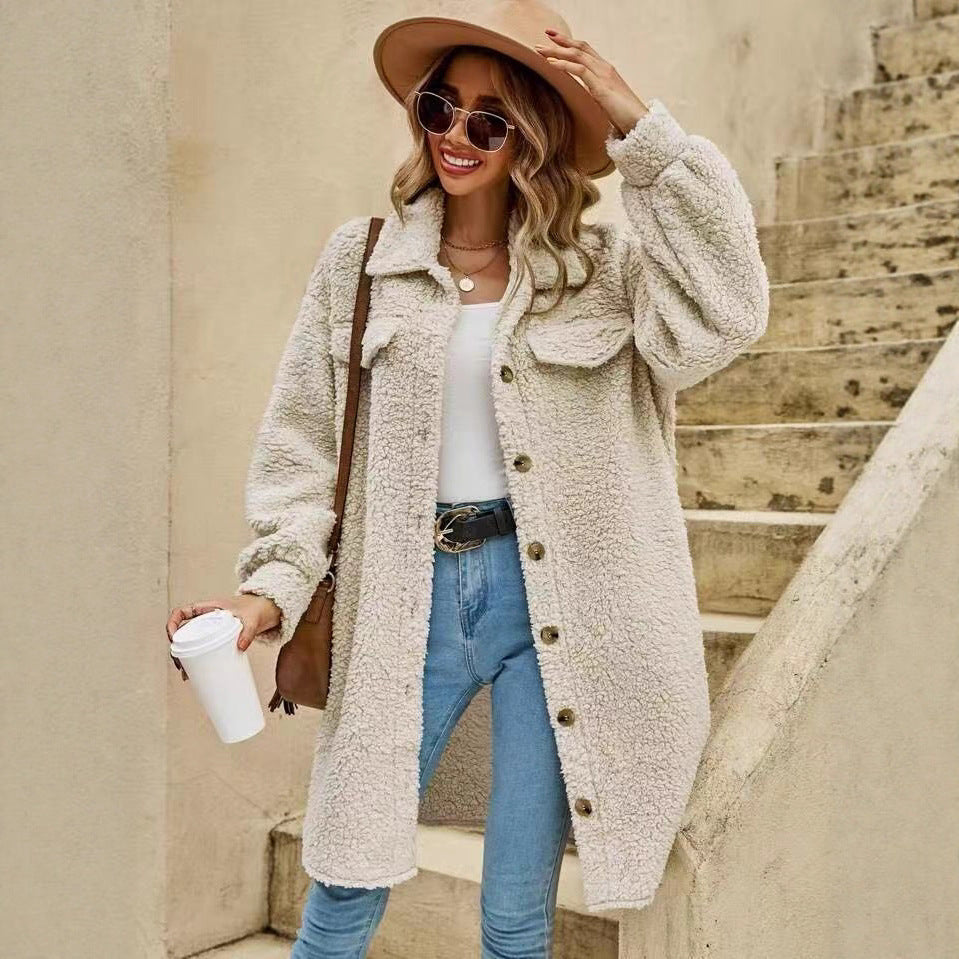 Woman wearing a beige coat, blue jeans, and a wide-brimmed hat, standing on steps.