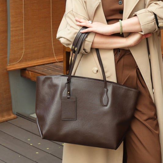 Person holding a brown leather tote bag outdoors