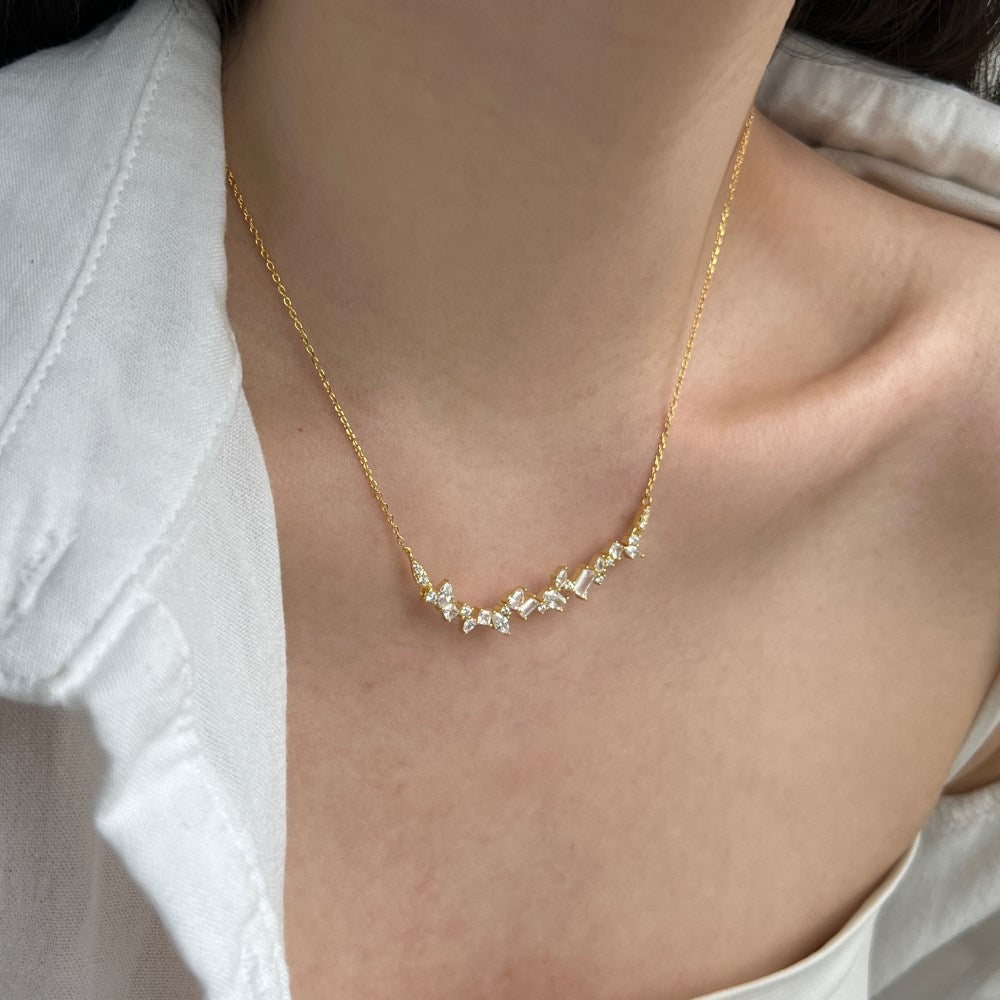 Gold necklace with small diamonds on a person wearing a white shirt.
