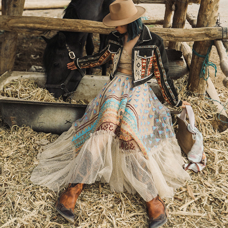 Person in a patterned dress and cowboy hat interacting with a horse in a rustic setting.