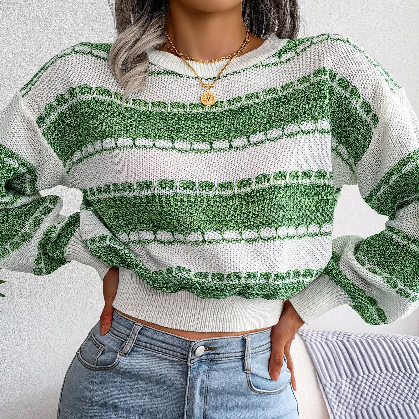 Person wearing a green and white patterned sweater and blue jeans indoors.
