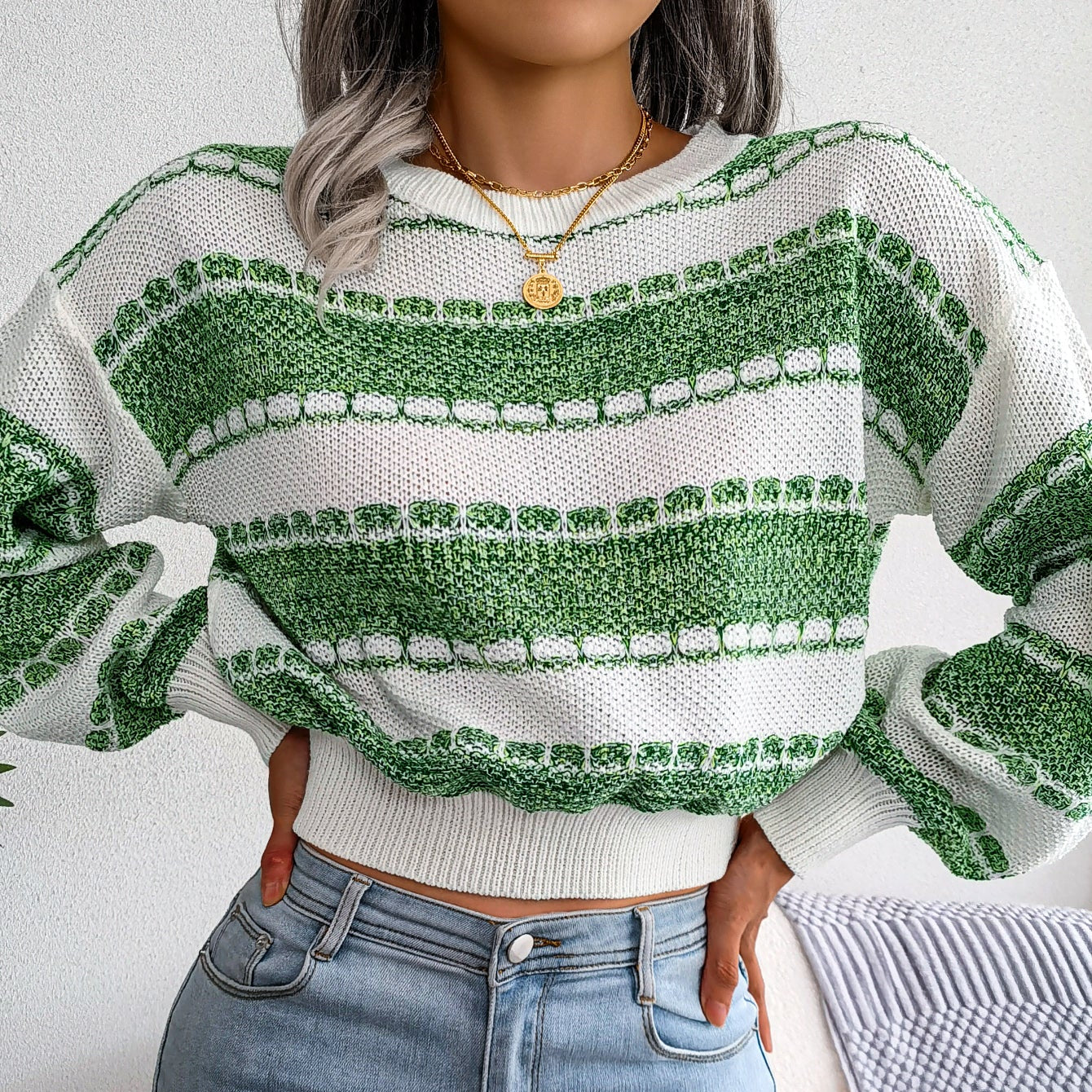 Person wearing a green and white patterned sweater and blue jeans indoors.