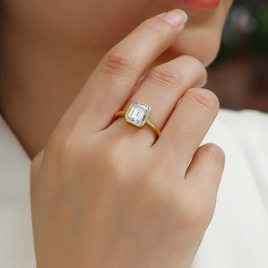 Close-up of a hand wearing a gold ring with a diamond on a blurred background