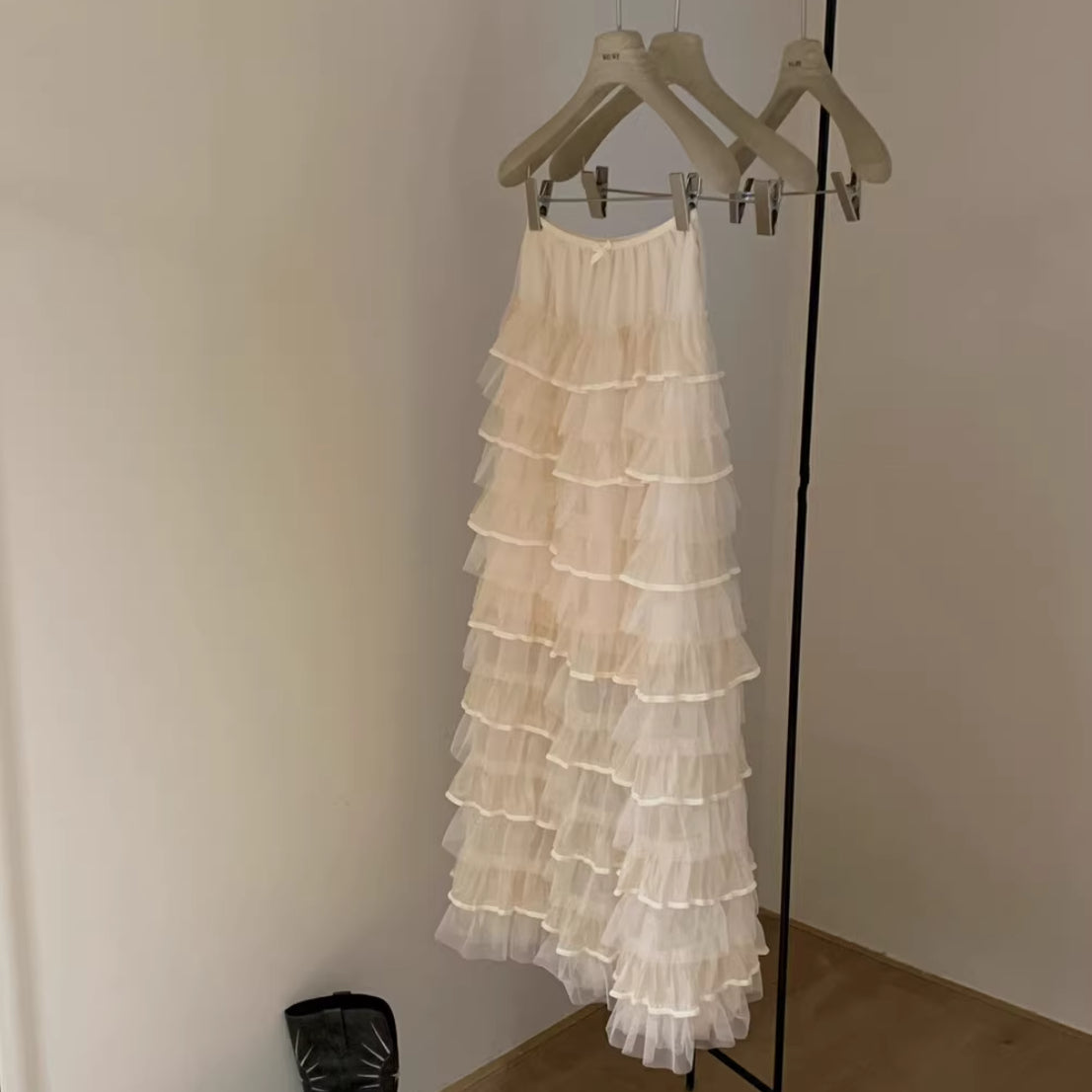 Beige tiered dress hanging on a rack against a plain wall.
