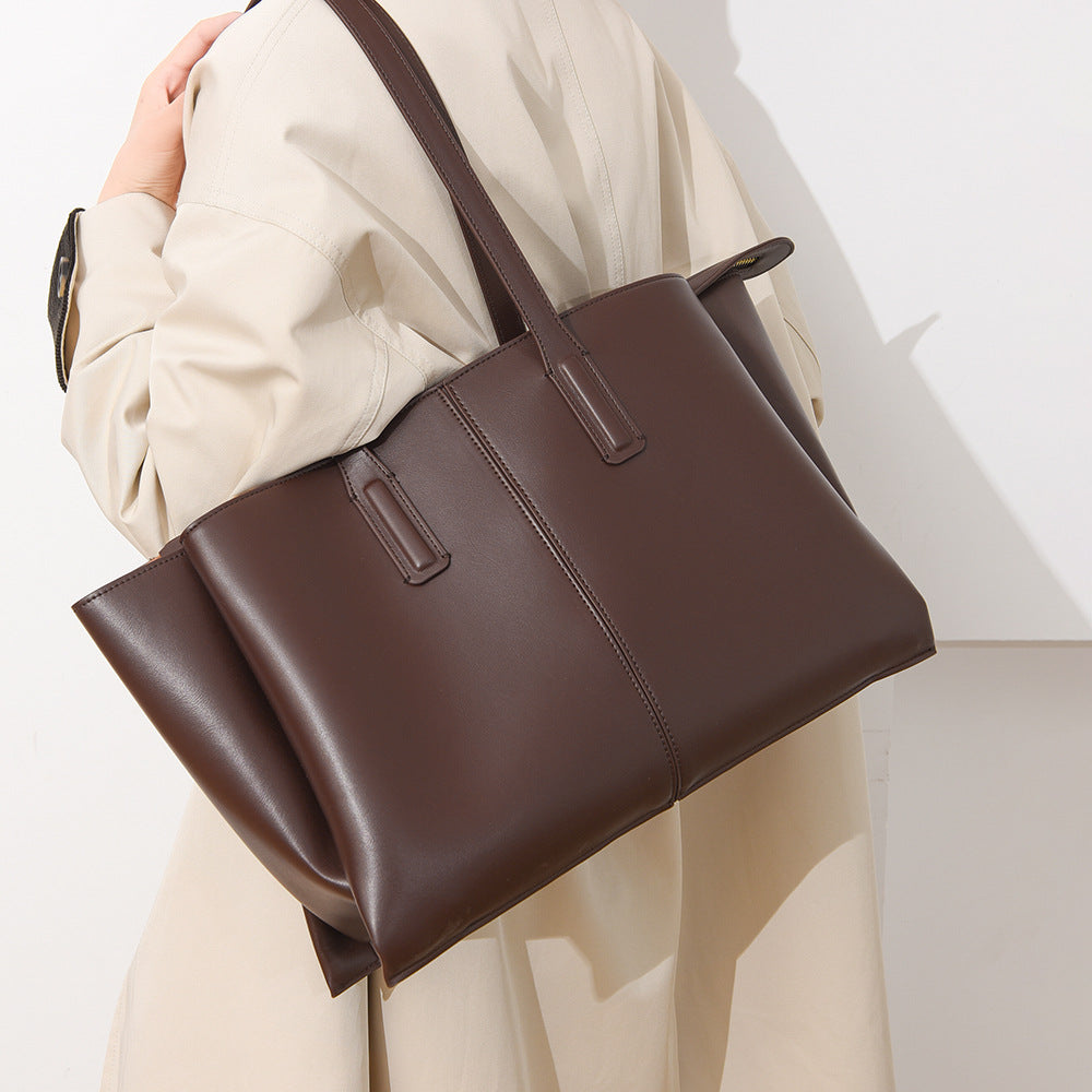 Brown leather handbag held by a person wearing a beige coat on a light background