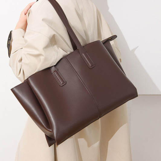 Brown leather handbag held by a person wearing a beige coat on a light background